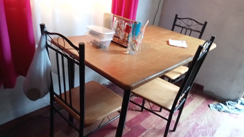 Real dining table with black metal chairs, a glass, stacked containers and red curtains.